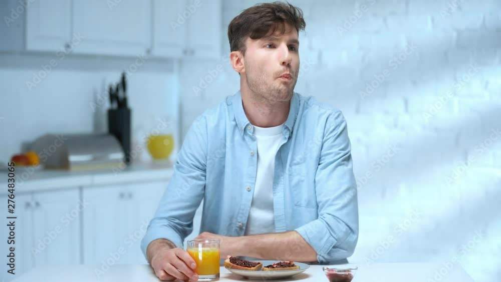 man eating bread toasts with jam, drinking orange juice, looking around and smiling in kitchen man eating bread toasts with jam, drinking orange juice, looking around and smiling in kitchen