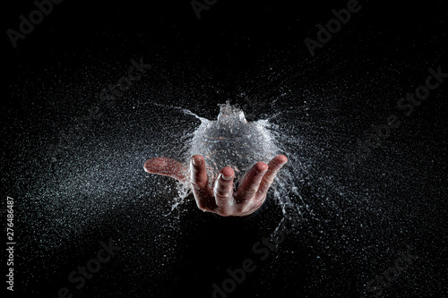 explosion of a balloon full of water held on a hand, black background studio shot.