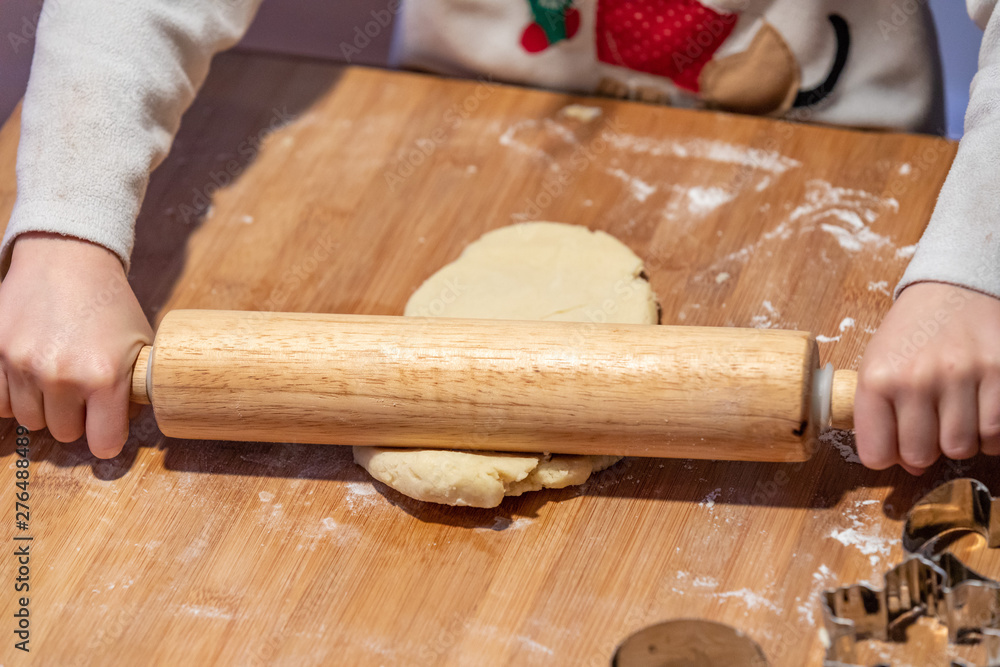 Kids hands rolling a piece of a cookie dough into a a thin pastry sheet using wooden roller pin. Kids hands rolling a piece of a cookie dough into a a thin pastry sheet using wooden roller pin.