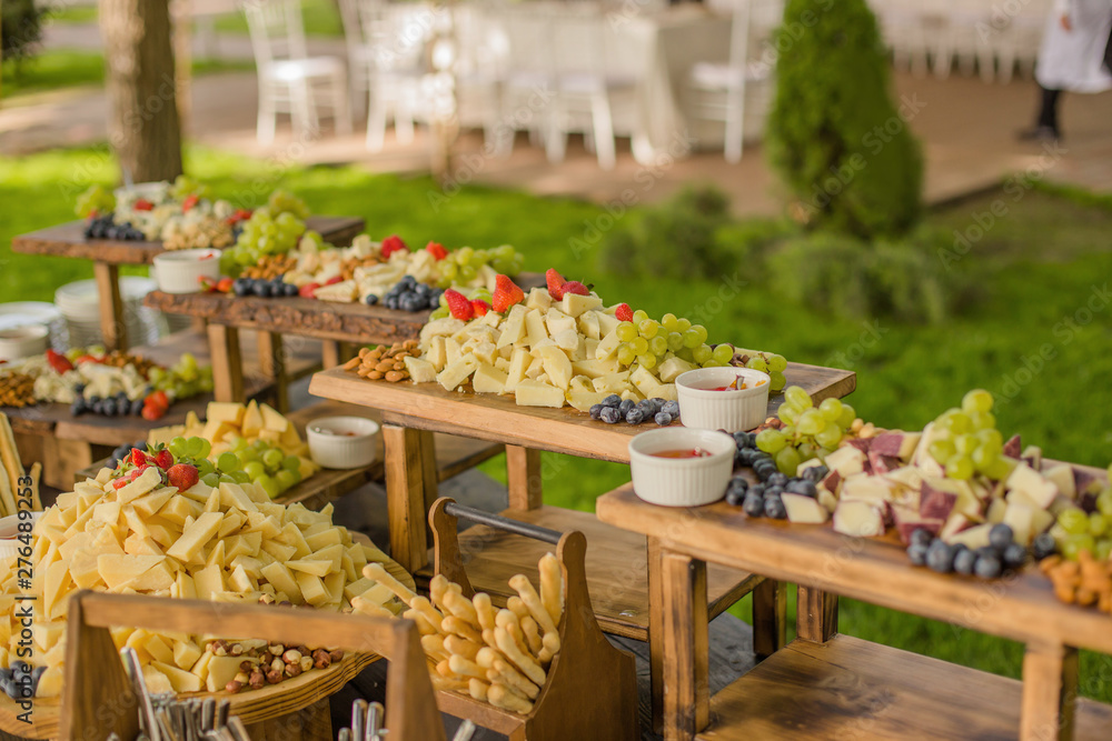 Food at the event, wedding reception with a variety of cheese, fruits, nuts and breads laid out on wooden stands