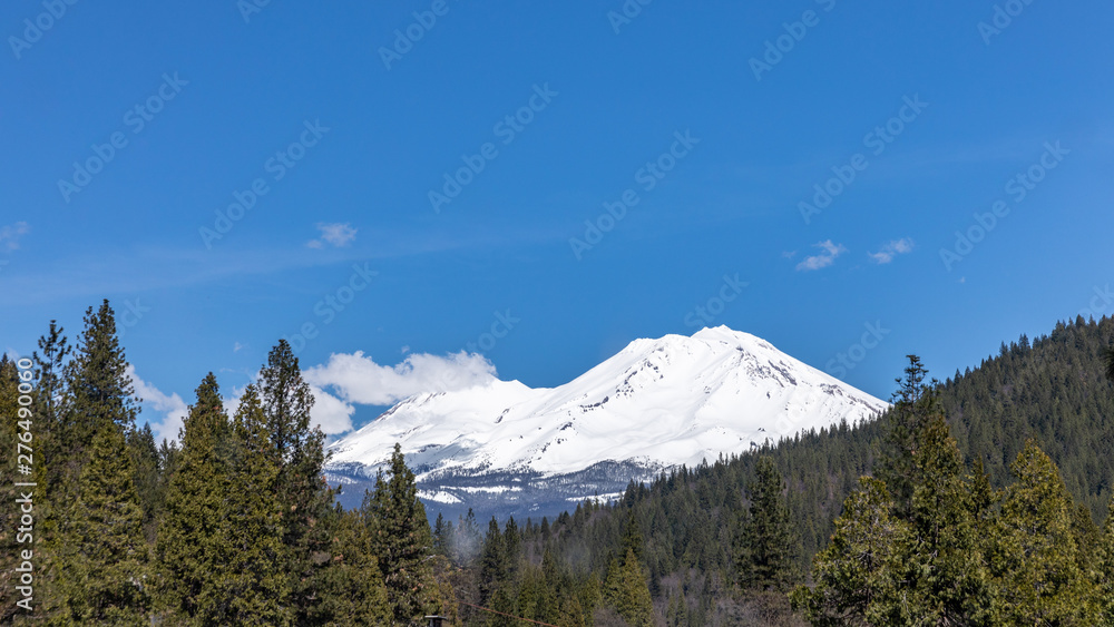Mount Shasta, California with clouds on a sunny day against bright blue sun