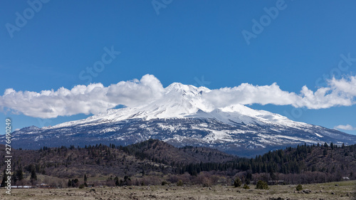 Mount Shasta, California with clouds on a sunny day against bright blue sun from I-5 interstate