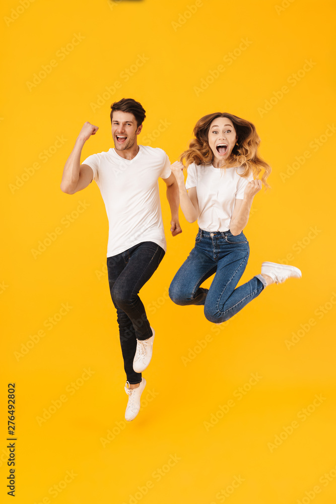 Full length portrait of beautiful couple man and woman in basic t-shirts rejoicing while clenching fists Full length portrait of beautiful couple man and woman in basic t-shirts rejoicing while clenching fists