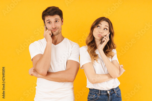 Portrait of happy couple man and woman in basic t-shirts standing together while talking on smartphones