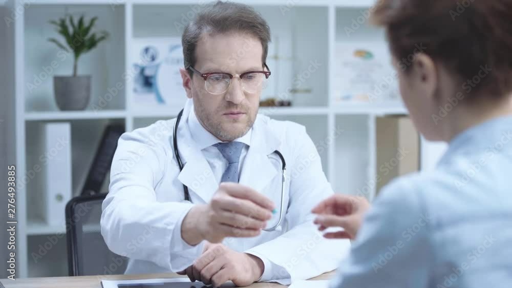 handsome doctor talking to nurse and giving her pill while sitting at workplace in hospital handsome doctor talking to nurse and giving her pill while sitting at workplace in hospital