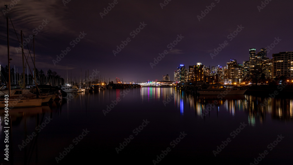 Vancouver, BC \ Canada - 13 March 2019: A night long exposure photo of marina inside Burrard Inlet of Vancouver Harbor with many yachts and boats. Lights of Canada place are in the background