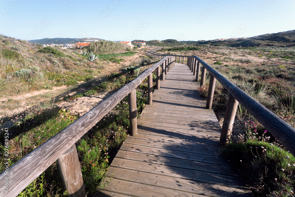 Wooden path from sunny beach to village through rural landscape, Portugal. Green hills in peaceful natural area of Algarve