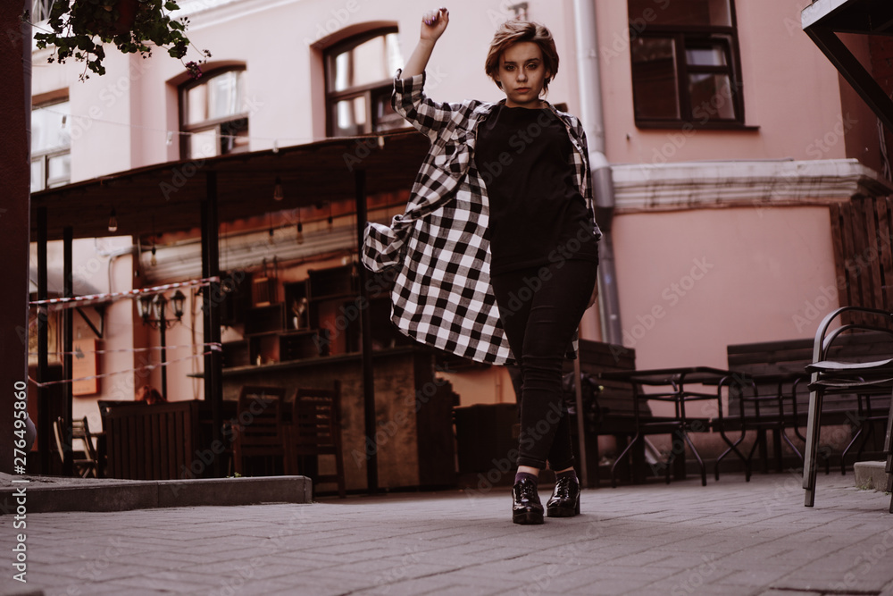 Beautiful young woman with short red hair in plaid shirt in the old city with red walls