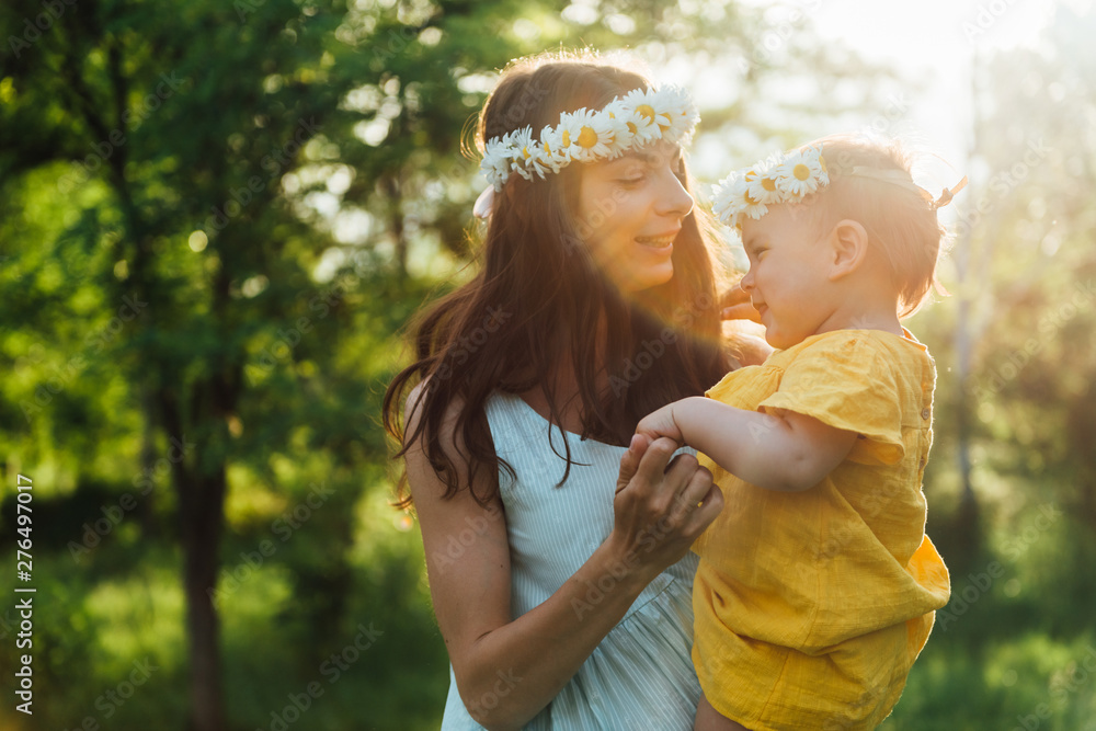 Happy mother with baby outdoors. Young woman and her child dancing during sunset with flowers