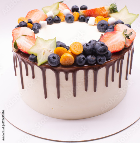 White cake decorated with white chocolate balls and berries: strawberries, blueberries, carambola, physalis. On a white background.