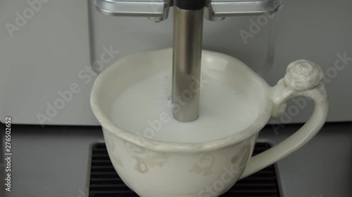 Preparing cappuccino by milk frothing pouring coffee steam from coffee machine into porcelain cup