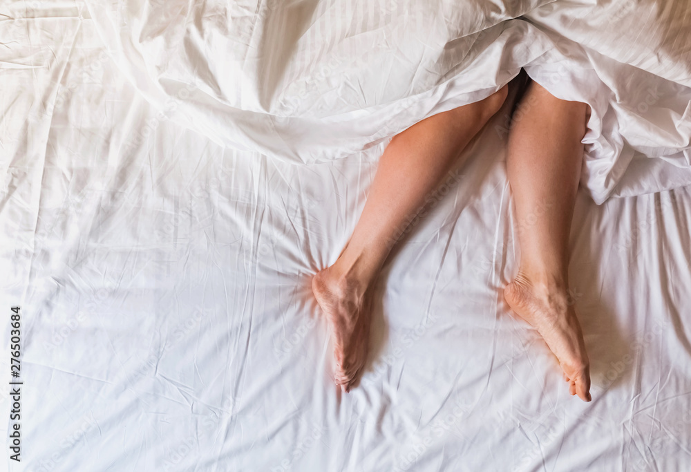 Woman's legs on the bed with white bedding, Woman's legs on the bed with white bedding,
