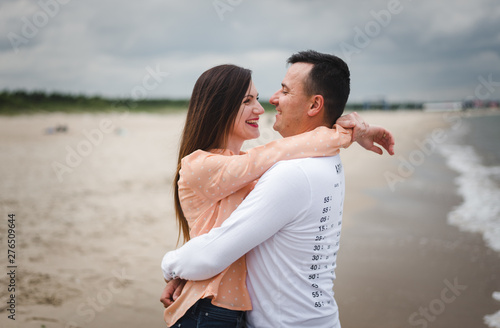 Couple in love enjoying vacation and having fun near sea. Young happy family walking on beach. Man and woman embracing and holding hands. Lovers walk on the sand. Romantic concept