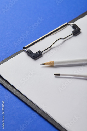 close up view of pencil and thermometer on clipboard isolated on blue