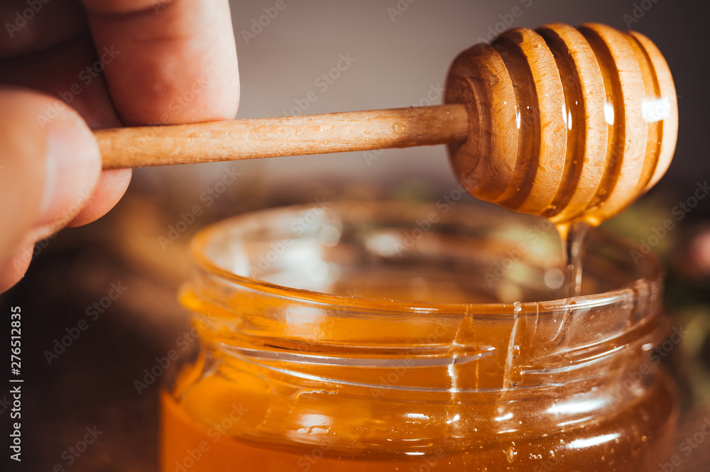 Fresh summer honey in glass jar and wooden honey dipper on rustic background Fresh summer honey in glass jar and wooden honey dipper on rustic background