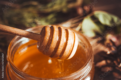 Fresh summer honey in glass jar and wooden honey dipper on rustic background
