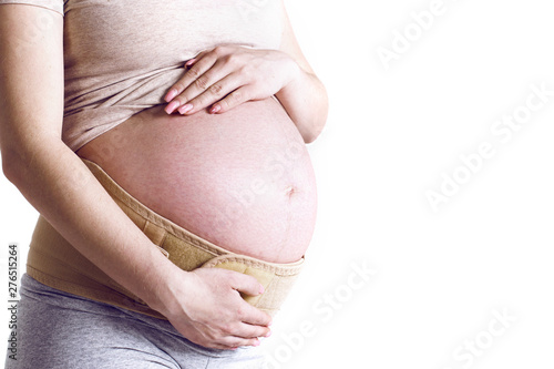 Close up of pregnant woman touching her belly on beige background. Pregnancy, maternity, preparation and expectation concept