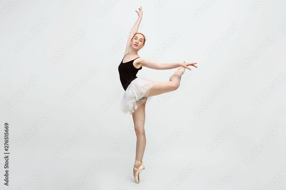 Young and incredibly beautiful ballerina is posing and dancing in a light grey studio full of light. The photo greatly reflects the incomparable beauty of a classical ballet art. Copy space