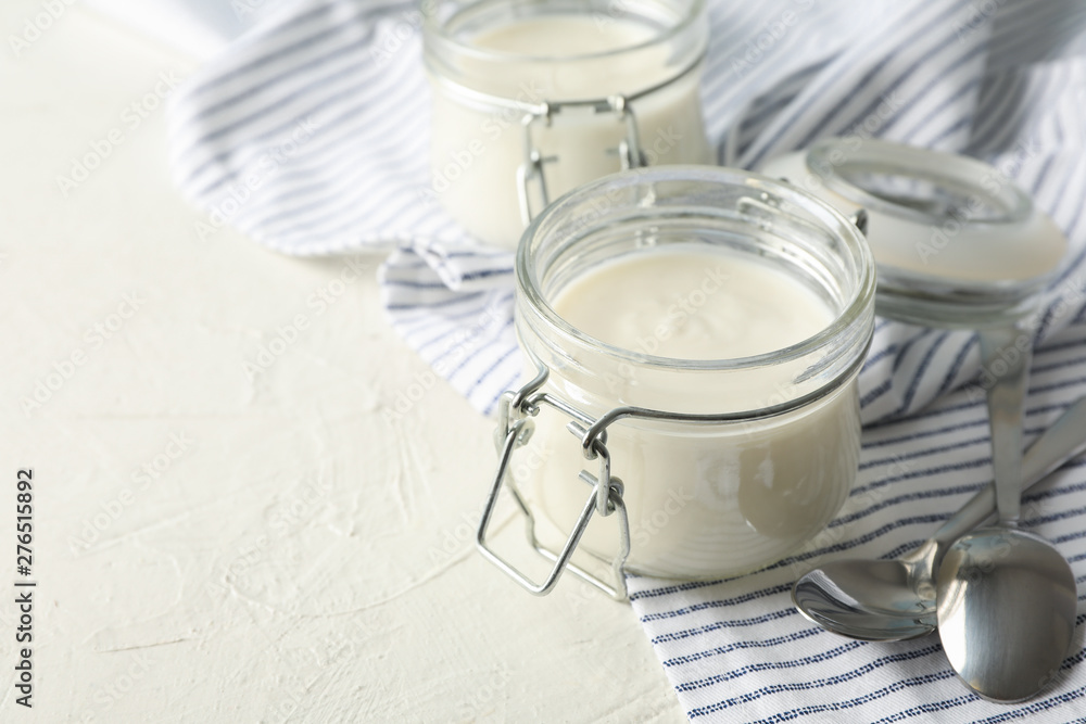 Glass jars with sour cream yogurt, spoons and towel on white cement background Glass jars with sour cream yogurt, spoons and towel on white cement background