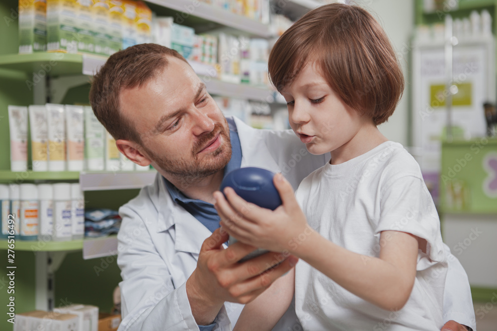 Close up of a mature male pharmacist helping little boy choosing shampoo to buy. Cute little boy talking to the chemist, shopping at drugstore Close up of a mature male pharmacist helping little boy choosing shampoo to buy. Cute little boy talking to the chemist, shopping at drugstore