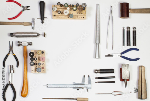 Top view of hands holding goldsmiths tools, jewelry objects. Tools over white background.