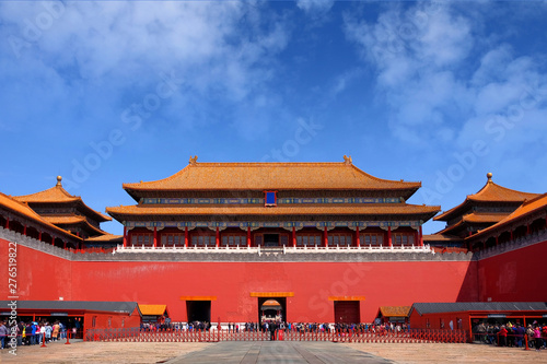 People queuing in front of one of the internal red colored gates of the Palace Museum, known as the Forbidden City, in Beijing, against a blue sky.