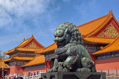 Marble lion statue inside the Palace Museum in Beijing, against red buildings with orange roofs, with a blue summer sky in the background.