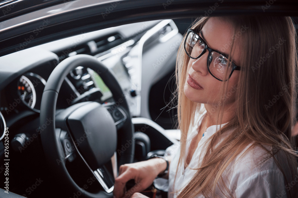 Dreamy look. Beautiful blonde girl sitting in the new car with modern black interior Dreamy look. Beautiful blonde girl sitting in the new car with modern black interior
