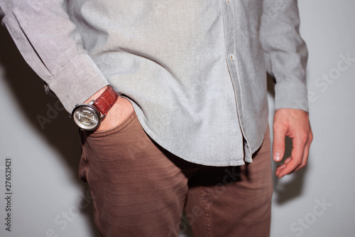 Closeup fashion image of luxury watch on wrist of man.body detail of a business man.Man's hand in beige pants pocket closeup at white background.Man wearing brown jacket and white shirt.Not isolated