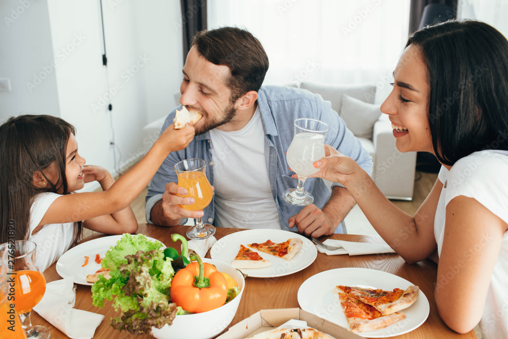Family enjoying pizza lunch. Father, mother and daughter during dinner.Yammy, it's very tasty piece of pizza Family enjoying pizza lunch. Father, mother and daughter during dinner.Yammy, it's very tasty piece of pizza