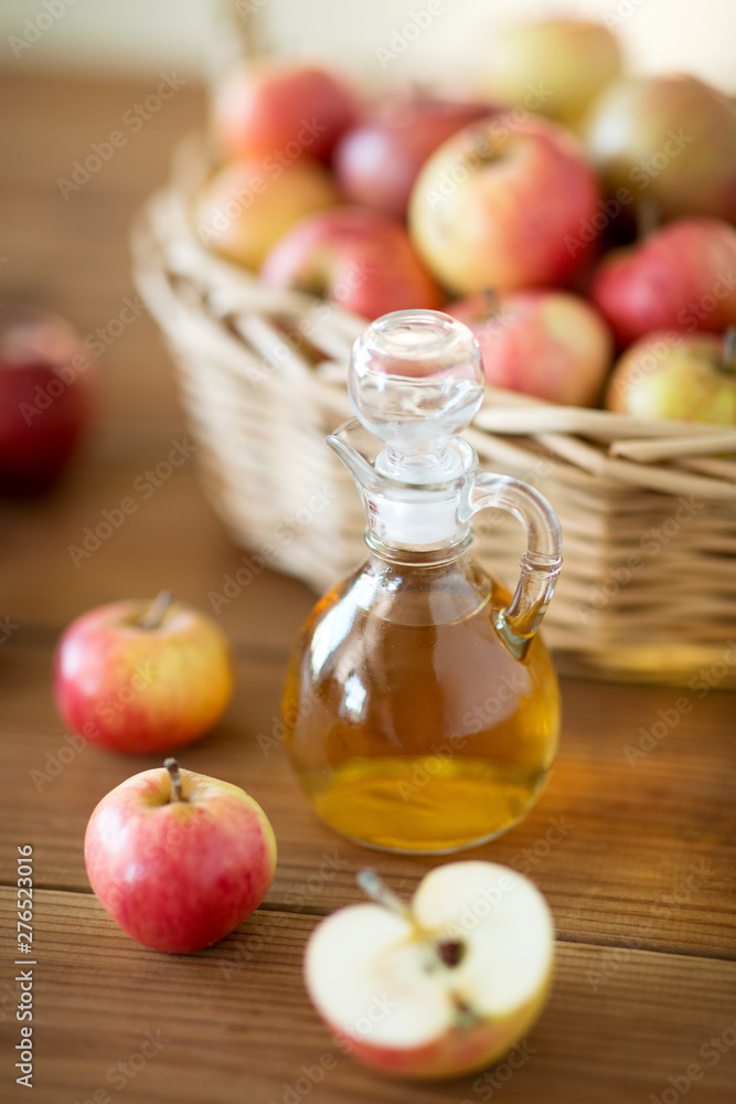 fruits, food and harvest concept - apples in wicker basket and glass jug of apple vinegar on wooden table fruits, food and harvest concept - apples in wicker basket and glass jug of apple vinegar on wooden table