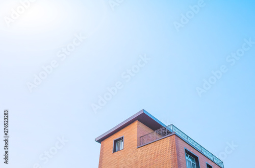 The roof of the house is pastel yellow and brown against a blue sky with light clouds. Bright sunny daylight. Place for text, minimalism. The concept of building houses, cottages. Copy space