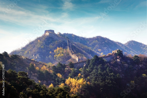 Panoramic view of the Great Wall of China, surrounded by green and yellow vegetation against a blue sky.