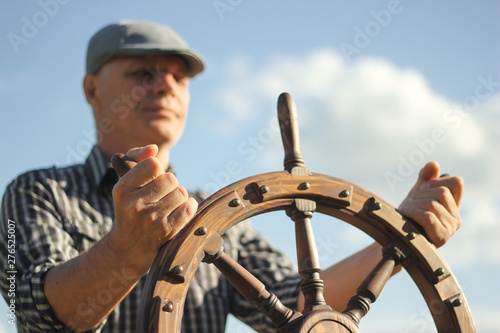 A man controls the yacht, hands on the steering wheel, handwheel on sky background