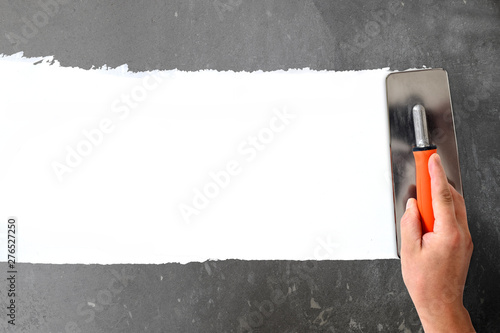 Hand with a spatula, the process of applying a layer of putty. Renovation of apartments. Repair the walls. Free space for advertising, text.