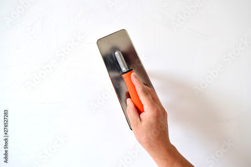 Hand with a spatula, the process of applying a layer of putty. Renovation of apartments. Repair the walls. Free space for advertising, text.
