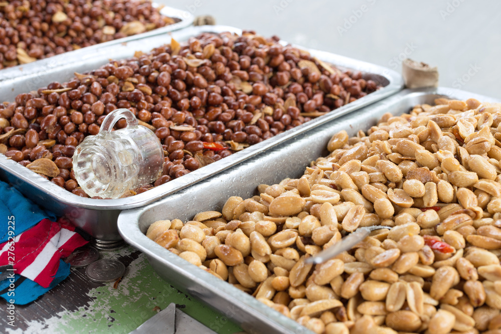 Roasted, salted peeled and unpeeled, crude peanuts on metal trays on the street market in the