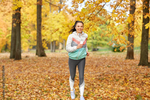fitness, sport, people and healthy lifestyle concept - young woman with earphones and smartphone running in autumn park