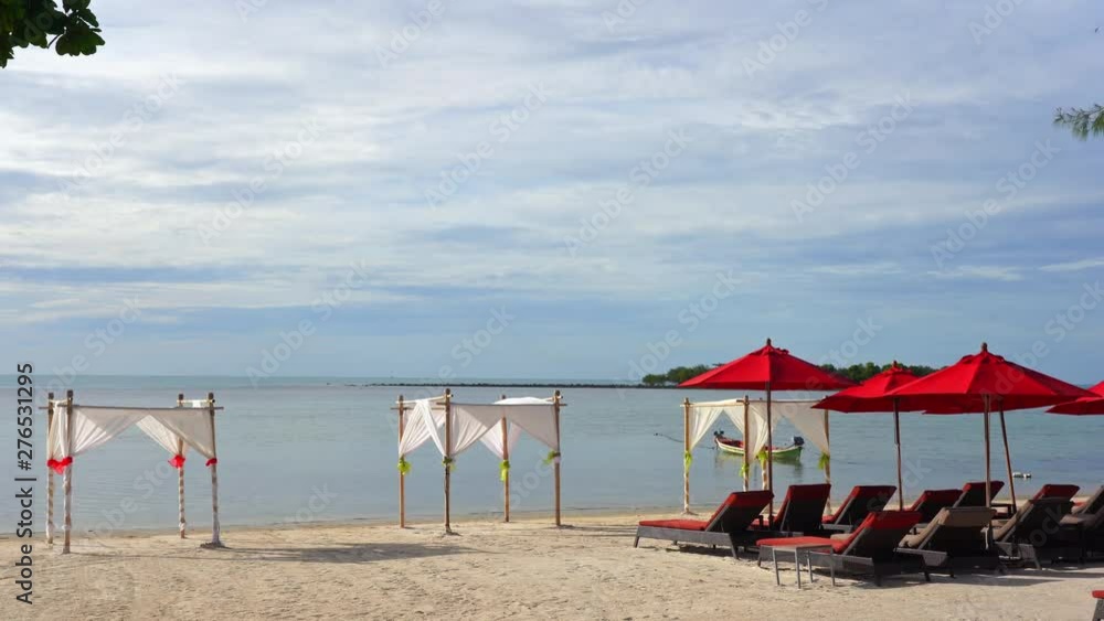 Static shot of beach sunbed loungers and red umbrellas and white gazebos on the beach