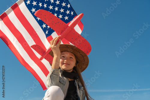 Independence Day.Beautiful girl in a cowboy hat on the background of the American flag is holding a red plane. USA celebrate 4th of July. photo