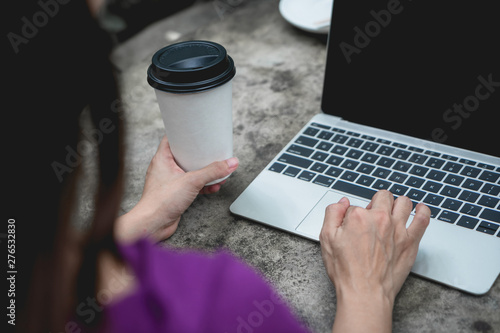 Business woman hands holding coffee cup and using laptop on table. Back view.