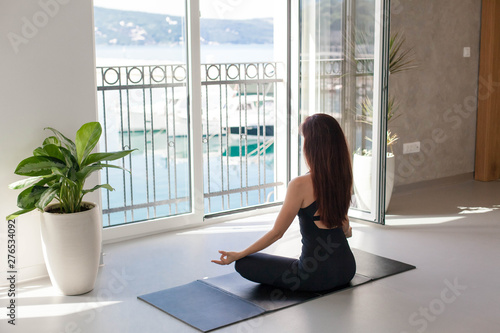 Young woman is practicing yoga in front of big opened window with view of sea beach, mountains. Girl is meditating. Sport workout in gym. Concept of healthy lifestyle, wellbeing. Female fitness class Free Download Young woman is practicing yoga in front of big opened window with view of sea beach, mountains. Girl is meditating. Sport workout in gym. Concept of healthy lifestyle, wellbeing. Female fitness class - GFXLoad