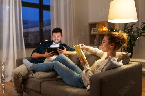 leisure and people concept - happy couple with tablet computer and book at home in evening