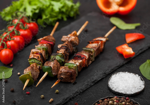 Grilled pork and chicken kebab with paprika on stone chopping board with salt, pepper and tomatoes on black background. Fresh lettuce and paprika pepper. Top view