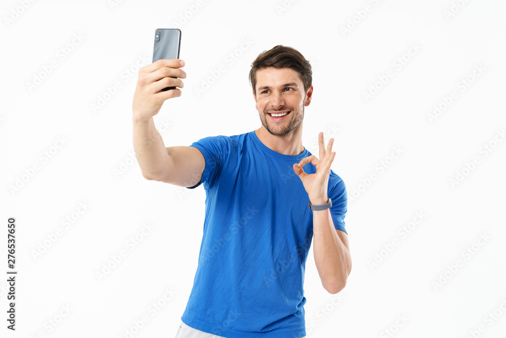 Photo of cheerful man in casual t-shirt showing ok sign and taking selfie on cellphone Photo of cheerful man in casual t-shirt showing ok sign and taking selfie on cellphone