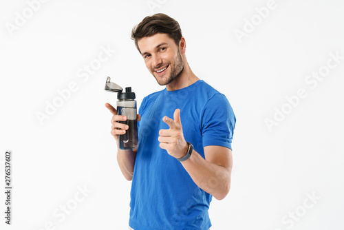 Photo closeup of cheerful man in casual t-shirt pointing finger at camera and holding water bottle