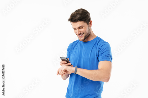 Photo of joyful man in casual t-shirt looking at wristwatch and holding cellphone