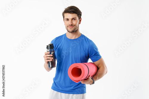 Photo of caucasian man wearing casual t-shirt smiling while carrying fitness mat and water bottle