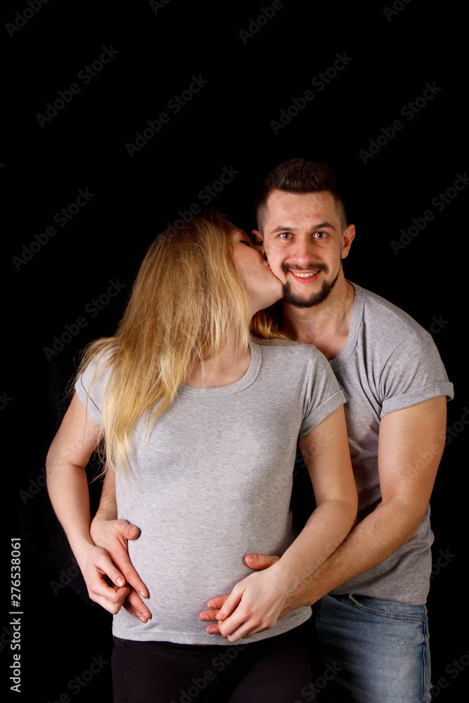 a man and a pregnant woman couple in their ninth month of pregnancy are embracing against an isolated black background. waiting for replenishment in the family a man and a pregnant woman couple in their ninth month of pregnancy are embracing against an isolated black background. waiting for replenishment in the family