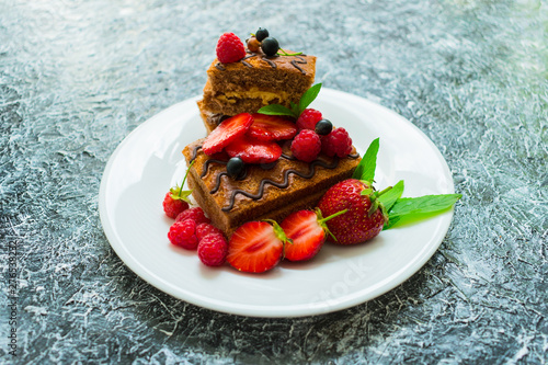  Chocolate sponge cake with cream and fresh berries. Summer dessert on a textured gray black background. Close-up.